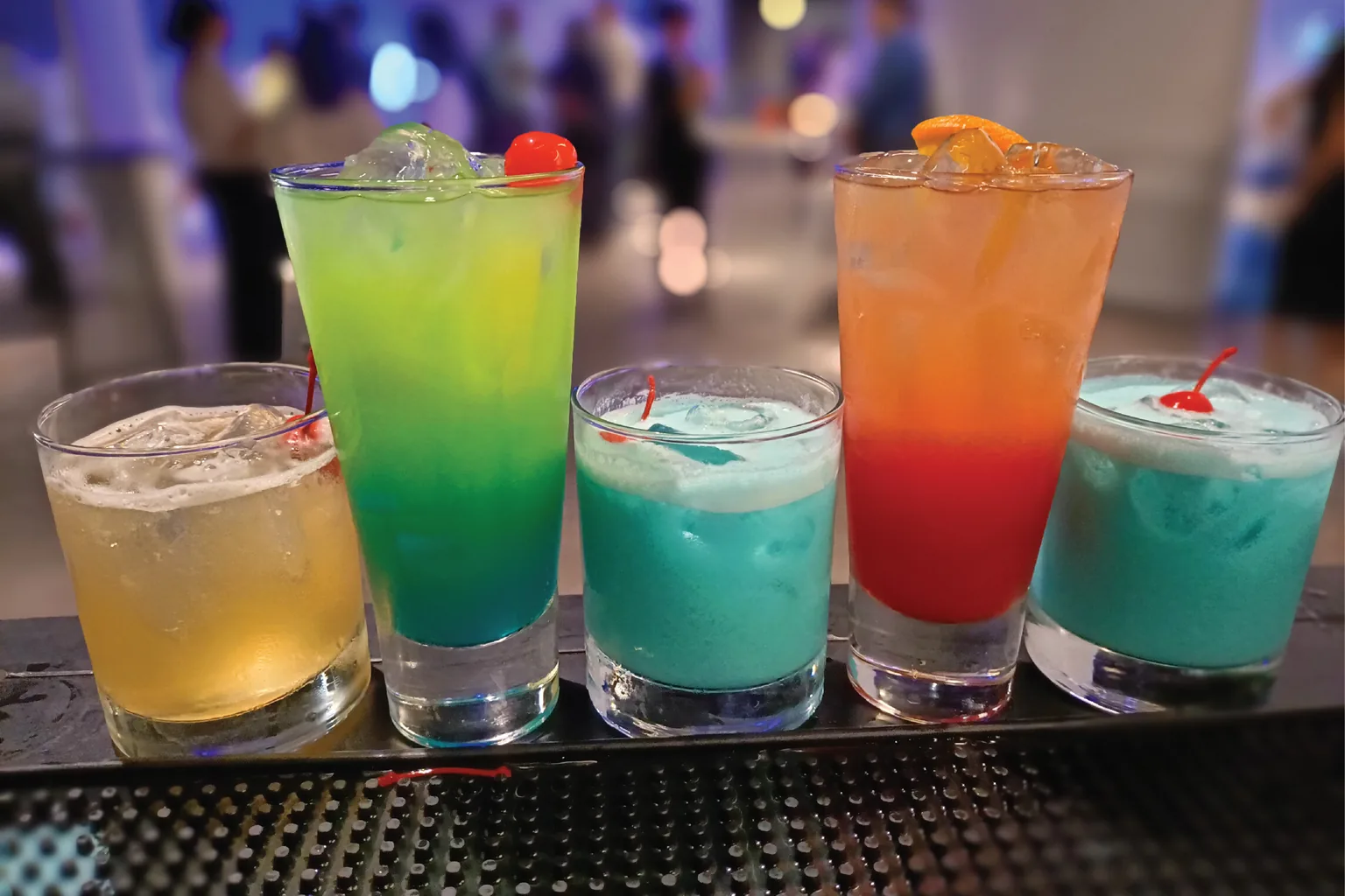 Three elegant cocktails on a candlelit event bar